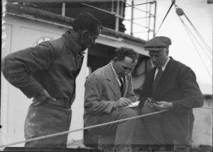 Three unidentified men writing in notebook on ship's deck