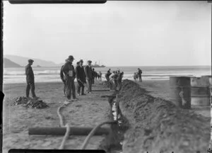 Unidentified men digging trench down beach towards sea, Lyall Bay, Wellington