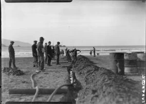 Unidentified men digging trench down beach towards sea, Lyall Bay, Wellington