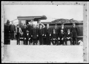 Group of 16 railway employees standing beside an early steam locomotive