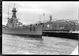 Warship & crowd at wharf, framework of wharf buildings behind