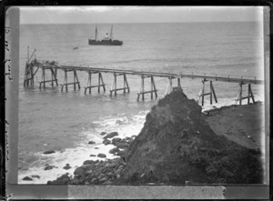 View of a two-masted steamship at sea; a rocky beach and pier in the foreground