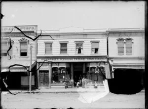 Premises of W Waring Taylor, ironmonger and iron merchant, Whanganui, with group of men and children outside and two women sitting in windows of upper storey