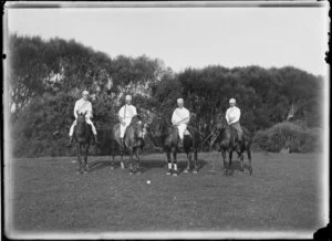 Four identified men on horseback and dressed for a game of polo and holding polo mallets, with a polo ball on the ground in front of the group, location unknown