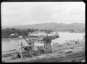 Steam crane and stacked wooden containers on Gisborne Wharf, including the Turanganui River, Turanganui Hotel, and moored ships, with the township and Turanganui bridge in the background