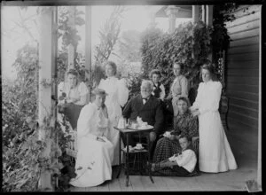 Group of unidentified people [a family?] on the verandah at Bradley's house, including a tea set on a stand, location unknown