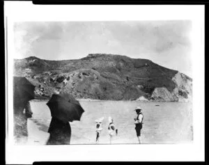Two unidentified girls and a man paddle in the water while two women with parasols watch, Kaiti Beach, Gisborne