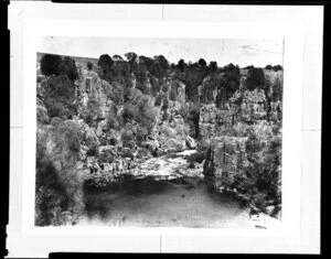 Group of unidentified people beside the Esk River, Tasmania; graffiti can be seen on the stone cliff