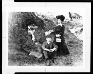 Three women and a man sitting and standing on a bank under a tree