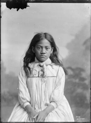 Studio portrait of unidentified Maori girl wearing white dress with scarf tied at neck