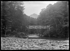 Bridge over a river flowing through beech forest, probably in the Otago region, circa 1926.