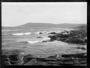 Unidentified rocky beach with a small town and wooded hills in the distance