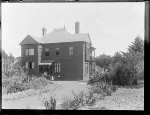 Two-storied wooden house, family group standing outside entrance