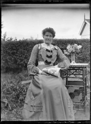 Unidentified woman sitting at a table in a garden, 1906.