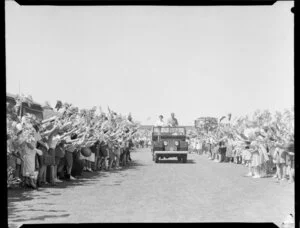Queen Elizabeth II and the Duke of Edinburgh standing in the back of a Land Rover as it drives past a crowd of children at Athletic Park, Wellington, Royal Tour 1953-1954