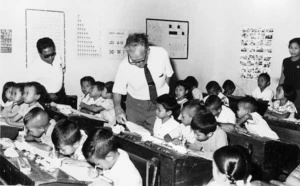 C E Beeby in an Indonesian classroom examining a student's work.