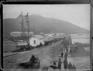 Crowd gathering in rain for reception of the Governor of New Zealand, David Boyle (7th Earl of Glasgow), at Gisborne wharf, including the Governor's ship, flags, horses and carts, and umbrellas