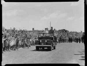 Queen Elizabeth II and the Duke of Edinburgh standing in the back of a jeep as it drives past a crowd of children at Athletic Park, Wellington, Royal Tour 1953-1954