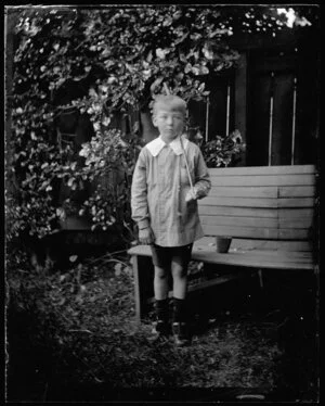 Small boy standing by garden seat