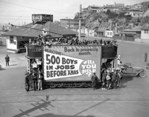 A tram, full with children, advertising the objective "500 boys in jobs before Xmas", Wakefield Street, with Oriental Parade in background