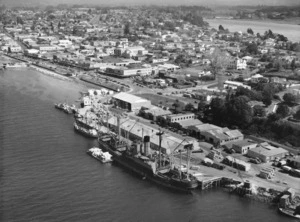 Aerial view of Tauranga showing a timber ship, wharves and the township - Photograph taken by Whites Aviation