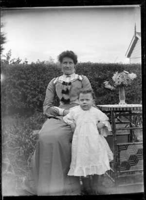 Unidentified woman sitting at a table in a garden, with a child, 1906.