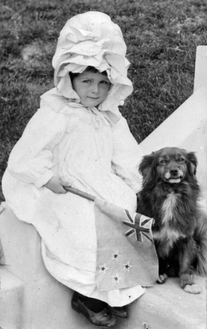 Dora Helyer, as a young girl, sitting next to a dog and holding a New Zealand flag