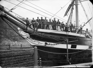 View of the prow of the sailing ship Margaret Galbraith in the graving dock at Port Chalmers, showing the figurehead, and crew members.