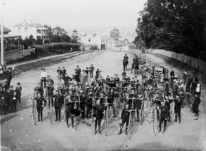 Group of uniformed men, each with a penny farthing bicycle, College Hill, Auckland