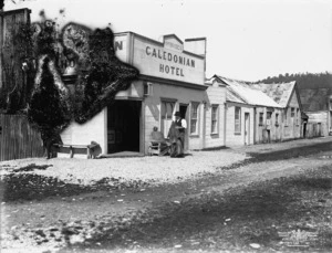 View of M McBrides' Caledonian Hotel, with older man out front, Okarito, Westland District