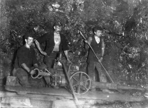 Three coal miners boring a hole down a mine