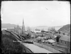 View of Port Chalmers wharves from the hillside above Ajax Road, with the new third Presbyterian church joined to the second church, on the left. Sailing ships and steamships berthed at the port, and one steamship sailing out, most of the ships flying flags for some ceremonial occasion, ca 1883.