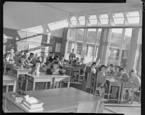 Children at desks in classroom drinking milk through straws