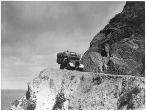 Truck of H W Thomas Ltd carrying wool bales on a steep coastal road, Cape Terawhiti, Wellington