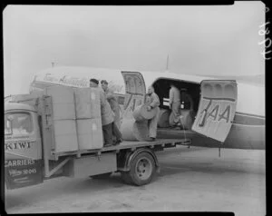 Men loading rolls of carpet from TAA plane to Kiwi Carrier truck at Wellington Airport