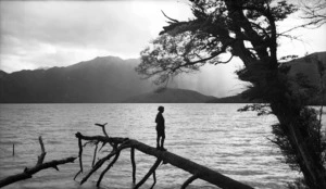 Woman standing on a fallen tree on the shores of Lake Hauroko, Southland