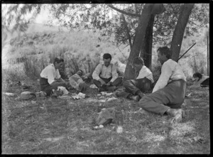 Group of men at rest, playing cards on the grass under a tree, on the Mendip Hills sheep farm.