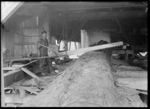 Creator unknown :Photograph of man standing next to saw inside timber mill