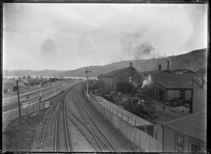View of Petone railway yards looking towards Wellington, with several steam locomotives, part of the workshops, and the main railway track leading south in centre foreground.