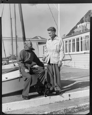 Men sitting next to yachts with dachshund