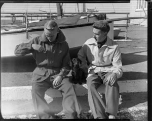 Men sitting next to yachts with dachshund