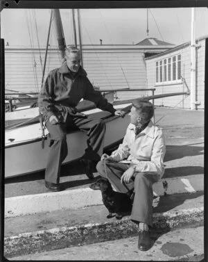 Men sitting next to yachts with dachshund