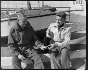 Men sitting next to yachts with dachshund