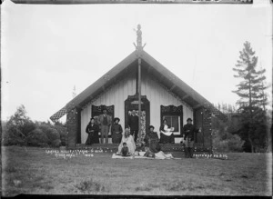 Group seated outside the carved meeting house at 'Marae-o-Hine' [Te Marae o Hinekakea], Riverhead, Auckland region