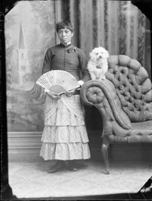 Unidentified woman with dog, wearing a plain top and skirt which is layered, holding an asian fan