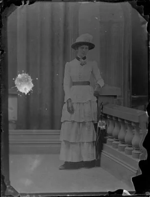 Unidentified woman with umbrella, wearing a hat and dress that has layers and is tight over the hips