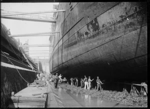 View of men working on the hull of a ship at an unidentified dry dock