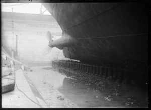 View of the hull of a ship looking towards a propeller, at an unidentified dry dock