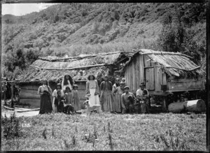 Maori family group in front of a whare and store house