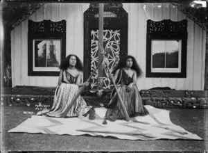 Maori women with taiaha seated in front of a meeting house
